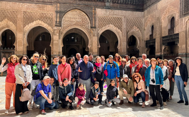 Un grupo diverso de personas posa para una foto en un patio histórico con arcos ornamentados. El ambiente es animado y alegre, reflejando un espíritu explorador.