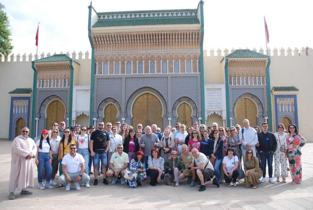 Un grupo de personas posa delante de un edificio tradicional ornamentado, con puertas doradas en arco y diseños intrincados. El ambiente es alegre y soleado.